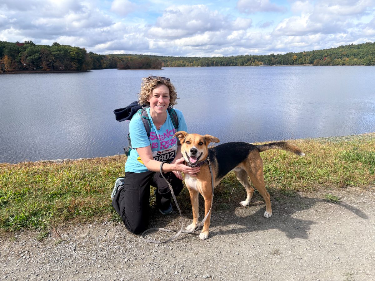 Alicia Weir kneeling with her dog Ziggy beside the water at Hopkinton State Park